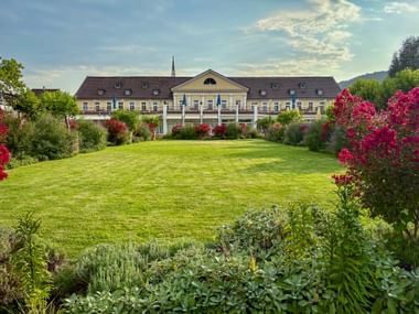 Kurhaus Bad Dürkheim, ein klassisches Gebäude mit Säulen, über einen gepflegten Rasen mit bunten Blütensträuchern und Gartenbeeten.
