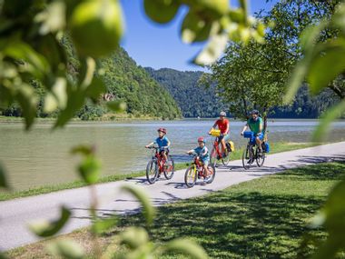 Familie auf Fahrrädern fährt entlang des Donauradwegs am Ufer der Donau
