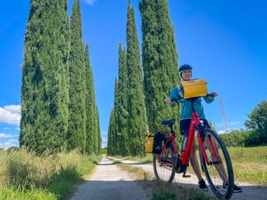 Radfahrerin am Feldweg zwischen Zypressen