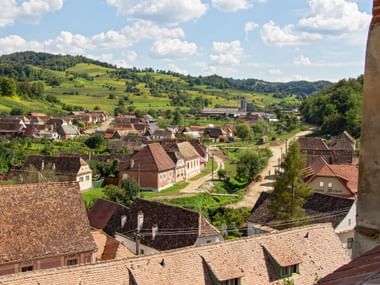 Aerial view of Biertan village in Romania with traditional houses, red-tiled roofs, and a church tower, surrounded by green rolling hills.