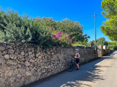 Radfahrerin an Steinmauer in Alcudia