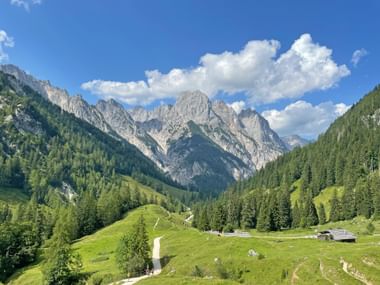 Panoramablick auf den Nationalpark Berchtesgaden mit dramatischen Kalksteingipfeln, grünen bewaldeten Tälern, Almwiesen und traditionellen Holzhütten.