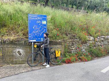 Cyclist stands on the side of the road in front of a map at Monte Berici.