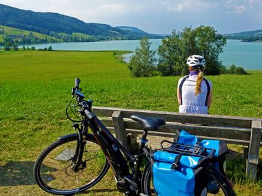 Radfahrerin auf Bank mit Ausblick auf einen See