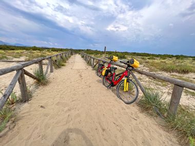 Two bicycles leaning against a wooden fence on the sandy beach