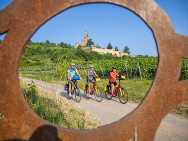Three cyclists in front of the Wachtenburg, framed by a steel work of art