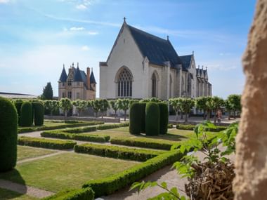 White Gothic chapel with pointed arch windows in Angers castle gardens. Formal garden with geometric hedges and trimmed trees in foreground.