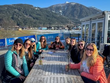 Gruppe von neun Frauen an Holztischen auf sonniger Terrasse mit Bergpanorama und Eurofun-Bannern beim Wintersporttag 2026.
