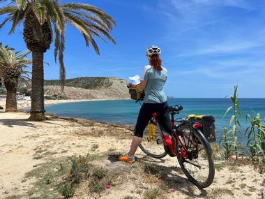 Radfahrerin beim Lesen der Reiseunterlagen an einem schönen Strand mit Palmen