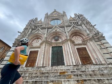 Radfahrerin blickt mit Satteltasche auf Dom in Siena