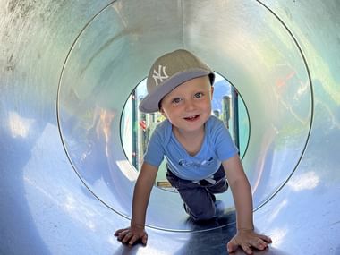 Kind krabbelt durch eine Röhre am Spielplatz in Bad Goisern