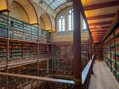 Innenansicht der Rijksmuseum-Bibliothek in Amsterdam mit raumhohen Bücherregalen, gewölbter Decke, Oberlicht und hohen Bogenfenstern.