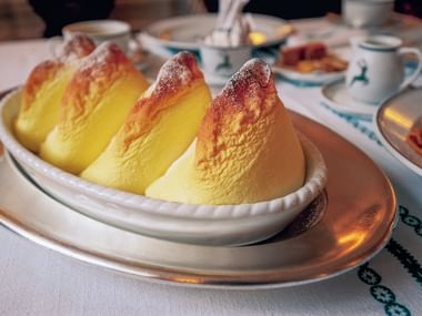Three golden soufflé dumplings dusted with powdered sugar on a white plate, traditional Salzburger Nockerl dessert served on a set table.