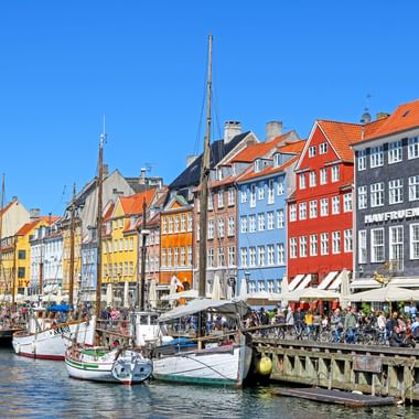 Historischer Nyhavn-Hafen in Kopenhagen mit bunten Giebelhäusern aus dem 17. Jahrhundert, Holzsegelbooten und Cafés am Wasser.