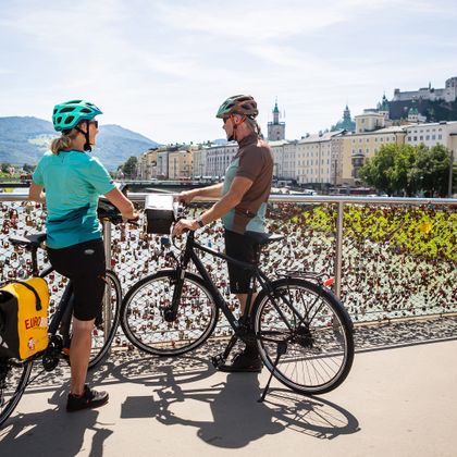 Stopover by two cyclists at the Makartsteg with a view of the old town and fortress of Salzburg