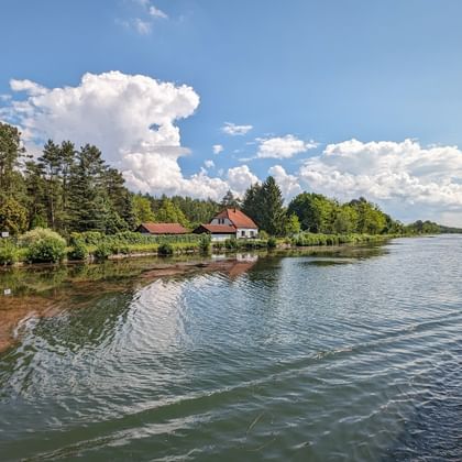View from MS Princess ship deck showing a calm waterway with houses and trees along the shore under a blue sky with white clouds.