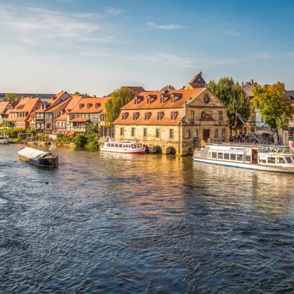 Historic waterfront of Bamberg's Little Venice with colorful half-timbered houses along the Regnitz River and tourist boats docked at the shore.