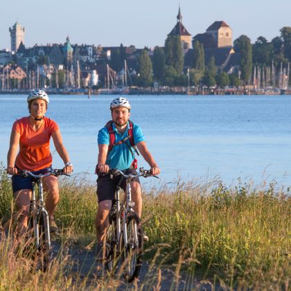 Two cyclists on a riverside cycle path, Arbon in the background