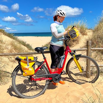 Radlerin steht am Strand an der Algarve mit ihrem Fahrrad