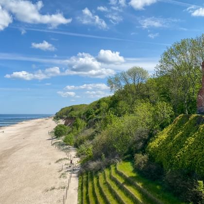 Red brick ruins of St. Nicholas Church on a coastal cliff in Trzęsacz, overlooking a sandy beach and the Baltic Sea under blue sky.