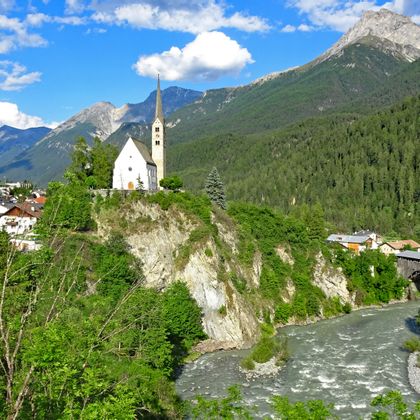 View of the mountain village of Scuol by a mountain stream, surrounded by forests and mountains