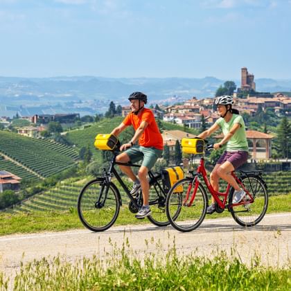 Zwei Radfahrer auf einem Radweg mit Montforte und Weinbergen im Hintergrund