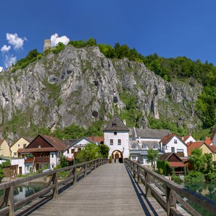 Eine Holzbrücke mit Blick auf Markt Essing im Altmühltal, im Hintergrund ein felsiger Hügel
