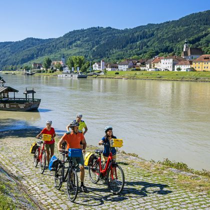 Cycling group leaving the bicycle ferry, in the background the departing ferry and the village of Engelhartszell.