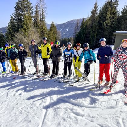 Gruppe von Skifahrern in bunter Winterkleidung posiert auf verschneiter Piste mit Wald und Bergen im Hintergrund beim Eurofun Touristik Wintersporttag 2026.