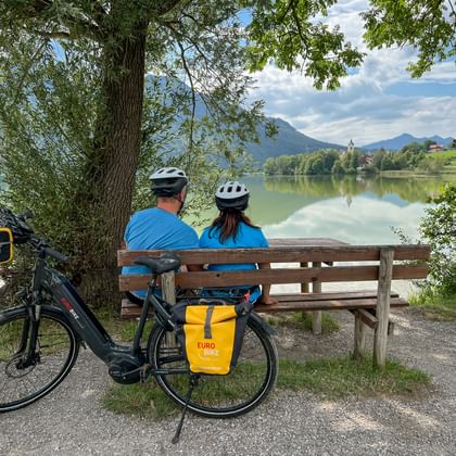 Radlerpaar sitzt auf Bankerl und blickt auf Weissensee