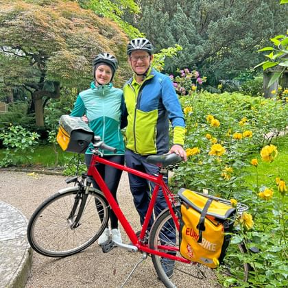 Cyclist and cyclist standing with bicycle in rose garden