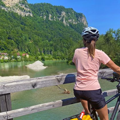 Radfahrerin bei der Pause auf der Draubrücke im Rosental, im Hintergrund bewaldete Berge
