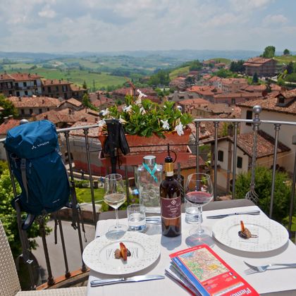 Blick von einer Restaurantterrasse auf die Altstadt Monforte d'Alba mit sanften Hügeln im Hintergrund