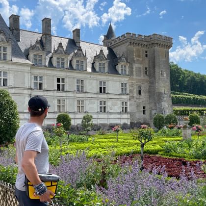 Radfahrer mit Helm betrachtet Schloss Villandry und seine Ziergärten mit bunten Blumenbeeten, geschnittenen Hecken und blauem Himmel.