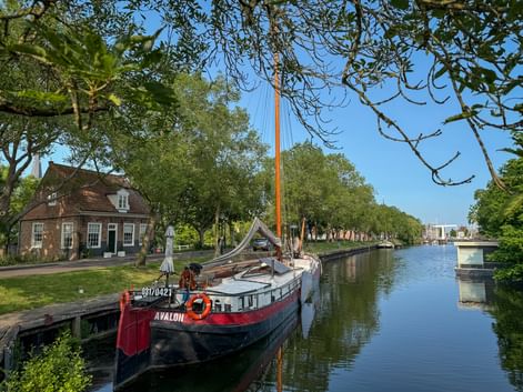 Traditional Dutch barge Avalon moored along a tree-lined canal in Enkhuizen with historic brick buildings and a bridge in the background.