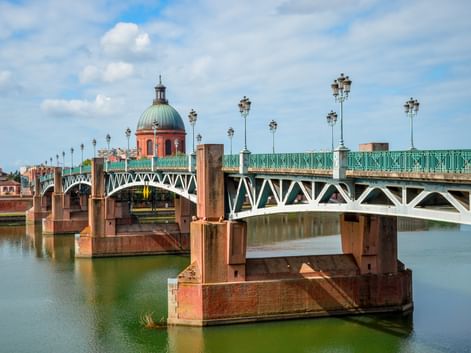 Pont Saint-Pierre Brücke mit grünem Metallgeländer und verzierten Laternen über der Garonne in Toulouse. Rosa Backsteinkuppel im Hintergrund.