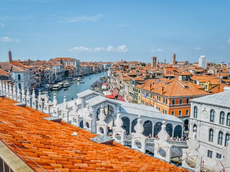 Panoramablick auf Venedigs Canal Grande mit der weißen Rialtobrücke, historischen Gebäuden mit Terrakottadächern und Booten auf dem Wasser.