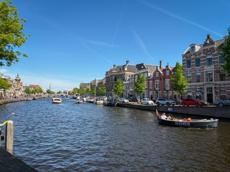 Der Fluss Spaarne in Haarlem mit traditionellen holländischen Häusern, am Kanal vertäuten Booten und einem vorbeifahrenden Ausflugsboot.