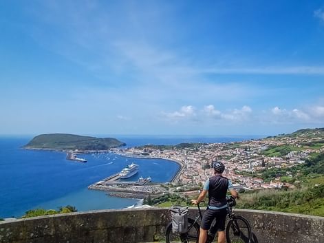 Radfahrer mit Fahrrad an Aussichtspunkt mit Blick auf Horta Hafen und Stadt auf den Azoren, mit Kreuzfahrtschiffen in der Bucht.