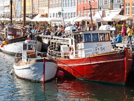 Traditional fishing boats moored in Nyhavn harbor, Copenhagen. Colorful historic buildings and outdoor cafes line the waterfront with visitors.