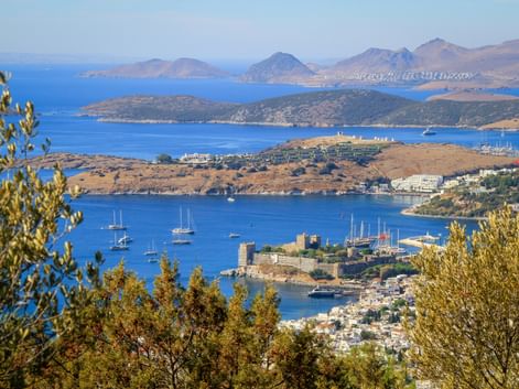 Luftaufnahme der Burg Bodrum und des Hafens mit Segelbooten im Golf von Gökova. Berge und Inseln in der Ferne unter blauem Himmel.