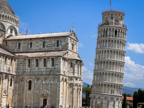 Der berühmte Schiefe Turm von Pisa und der Dom von Pisa mit weißen Marmorfassaden unter blauem Himmel in der Toskana, Italien.