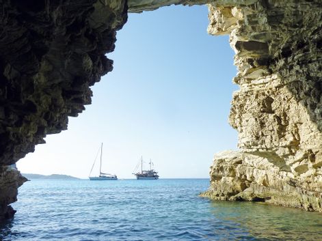 Blick aus einer Felshöhle auf zwei Segelschiffe am Meer
