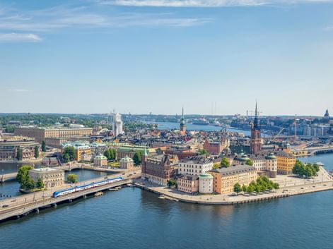 Panoramic view of Riga's historic Old Town on an island surrounded by water, with church spires, colorful buildings, and bridges under blue sky.