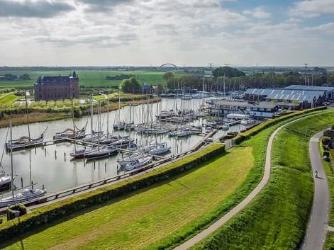 Luftaufnahme des Hafens von Muiden mit Segelbooten und Yachten entlang grüner Deiche. Historisches Schloss Muiderslot links sichtbar.
