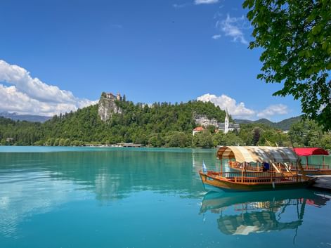 Traditional wooden boat on turquoise Lake Bled in Slovenia with Bled Castle on forested cliff and white church spire visible on shore.