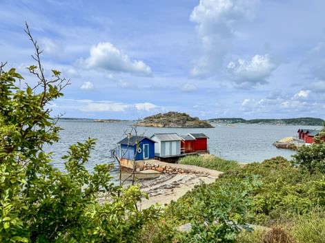 Colorful boathouses in blue, white and red on rocky shore at Brottkärs, Sweden. Calm water with small islands under cloudy sky.