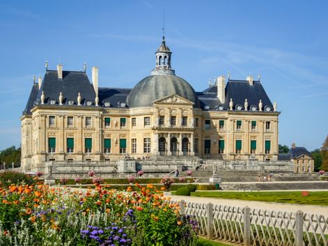 Château de Vaux-le-Vicomte with its distinctive dome and classical French architecture, surrounded by formal gardens with colorful flowers.