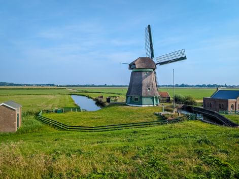 Dutch windmill in Schellinkhout surrounded by green polder landscape with canal and farm buildings under blue sky in North Holland.