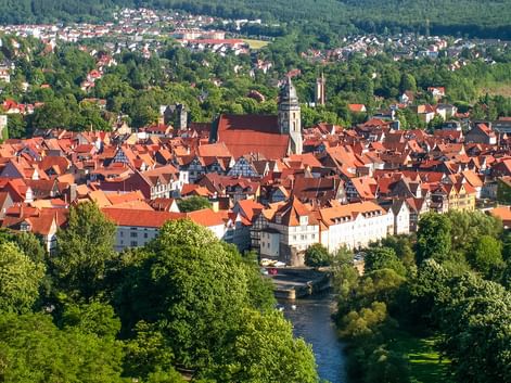 Aerial view of Hann. Münden old town with red-tiled roofs, church spires, and a river flowing through green landscape.